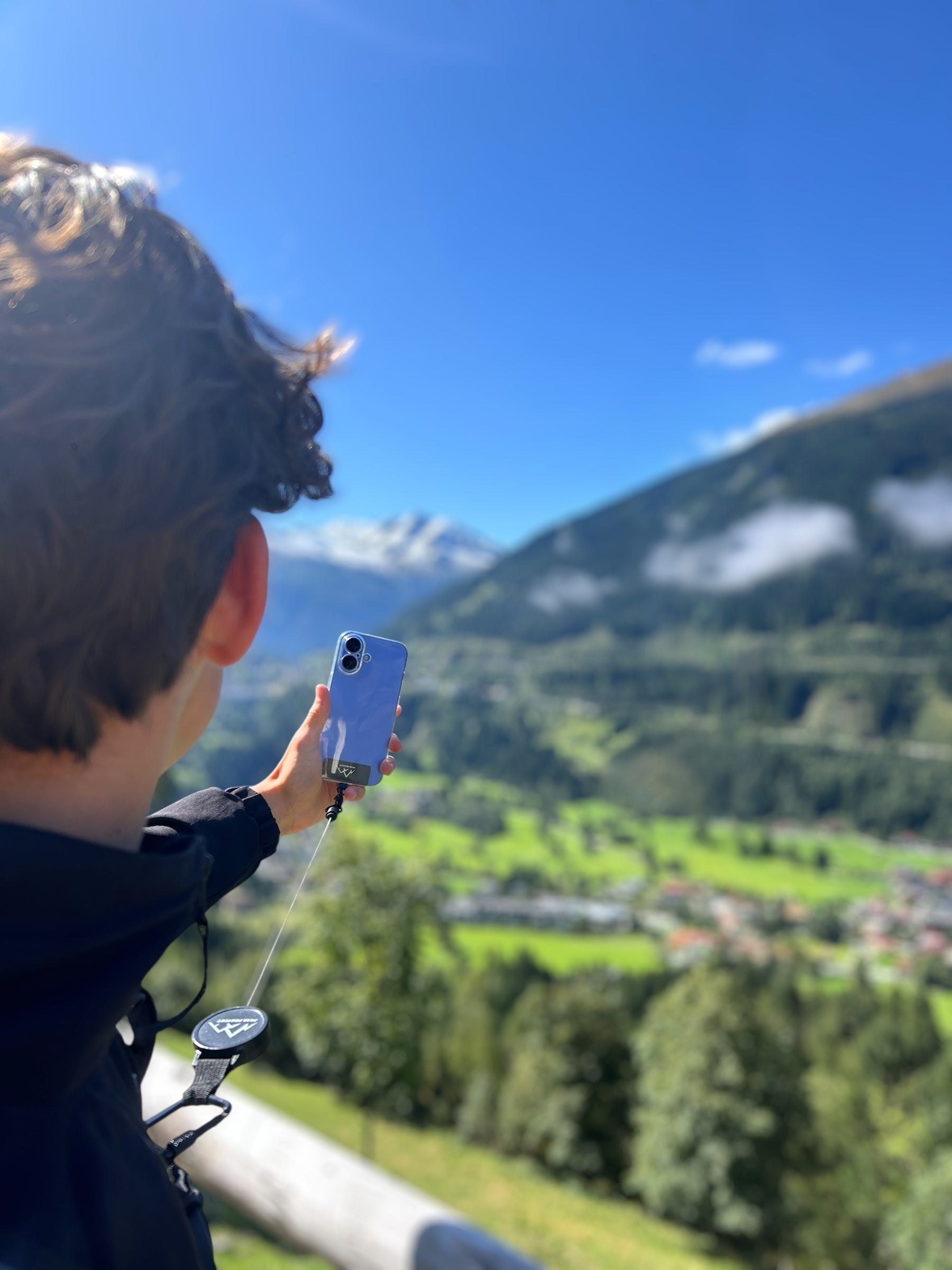 Person nutzt die Easy Protect Smartphone Sicherung mit ausziehbarem Metallseil beim Fotografieren einer Berglandschaft.