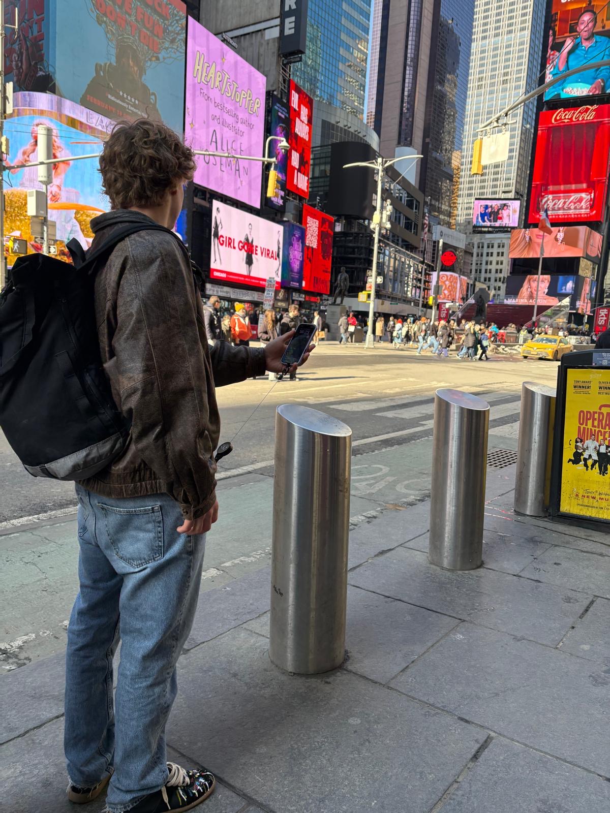 Person nutzt die Easy Protect Smartphone Sicherung mit ausziehbarem Metallseil beim Fotografieren in einer belebten Stadt.