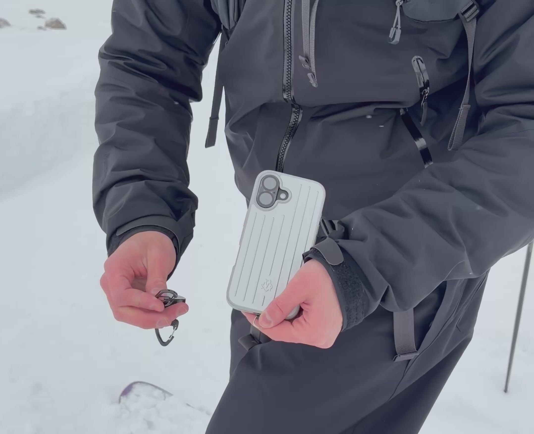 Video laden: Person verbindet die Easy Protect Smartphone Sicherung mit dem Karabiner am Smartphone im Schnee.