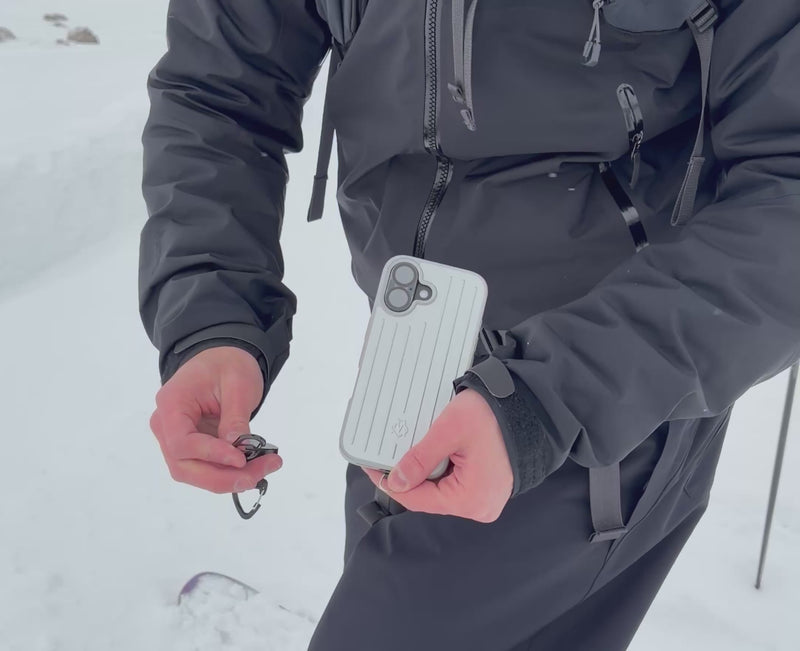 Person verbindet die Easy Protect Smartphone Sicherung mit dem Karabiner am Smartphone im Schnee.